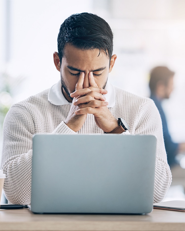 This image shows a man sitting at a desk with his hands clasped in front of his face, appearing stressed or deep in thought while working on a laptop. It visually reinforces the frustration and challenges mentioned in the accompanying text about the consequences of lacking a clear plan for your website, such as wasted resources and unsatisfactory results.